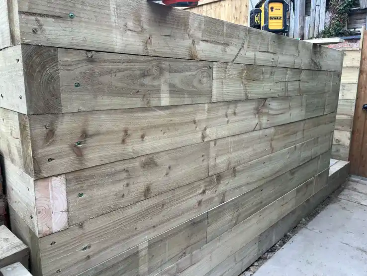 Sturdy wooden retaining wall constructed with pressure-treated lumber, perfect for creating level areas in sloped gardens.