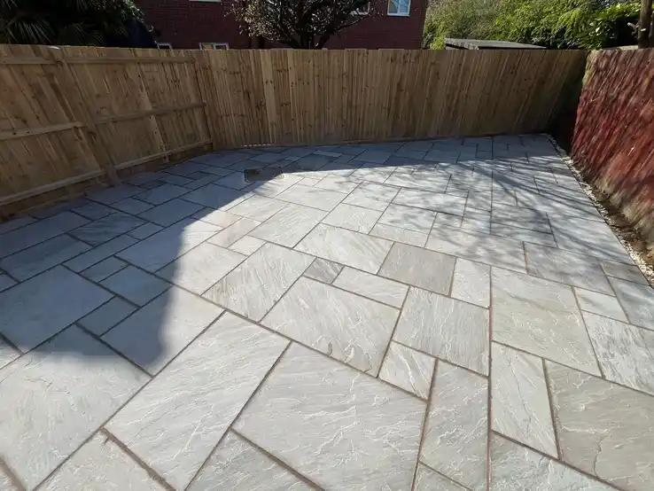 Elegant stone patio installation with complementary wooden fencing, creating a harmonious outdoor living area.