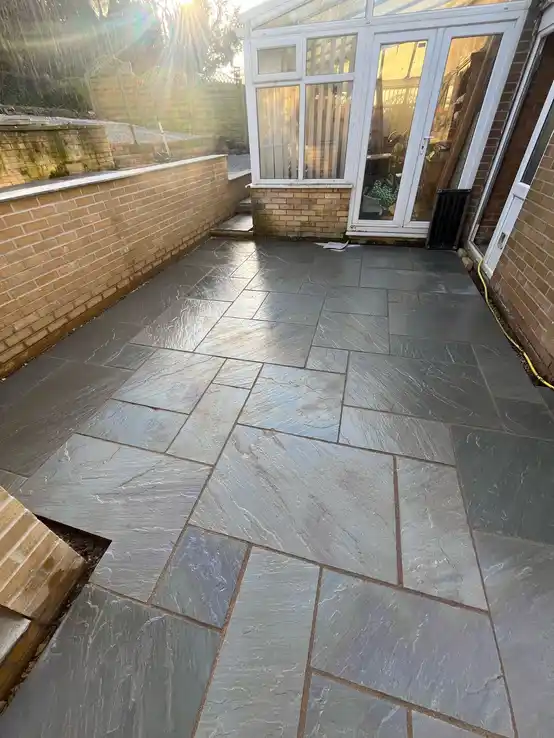 Gray stone patio installation adjacent to a conservatory, providing a seamless transition between indoor and outdoor spaces.